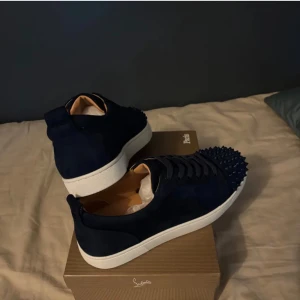 Mörkblå Christian Louboutin sneakers - Snygga mörkblå sneakers från Christian Louboutin i mocka med coola nitar på tån. Skorna har vita sulor, rund tå och klassisk snörning. Lyxig känsla och riktigt edgy look – perfekta för dig som vill sticka ut.