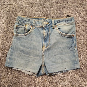 Jätte jätte tjusiga ljusblåa jeansshorts med broderi💞💞 -  Jätte snygga ljusblå jeansshorts med råa kanter och unika mörkblå broderade detaljer på fickor och linning. Klassisk femficksmodell med dragkedja och knapp. Perfekta för sommardagar när du vill sticka ut lite extra.🌸😽🍍💕