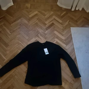 Svart långärmad tröja från Zara - En stilren svart långärmad tröja från Zara. Tröjan har en klassisk passform och är tillverkad i ett mjukt material som känns skönt mot huden. Perfekt att matcha med jeans eller linnebyxor för en clean look.