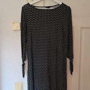 Svartvit blommig klänning Lindex XS - Supersöt svart klänning från Lindex i storlek XS med vitt blommönster. Modellen är kort med långa ärmar och knyt vid ärmsluten. Perfekt för dig som gillar en avslappnad men ändå stilren look. Tillverkad i mjukt material som känns skönt mot huden.