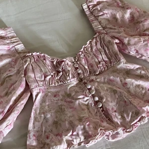 En blommig blus med puffärmar från For Love & Lemons  - Supersöt blommig blus i ljusrosa med romantiskt mönster och stora puffärmar. Toppen har knappar framtill, rynkade detaljer vid bysten och en lätt volangkant nedtill. Perfekt för dig som gillar en feminin och vintageinspirerad stil🌸Använd endast en gång! Säljer pga den har blivit för liten på mig. Köpt för 1200kr, Nypris: 700kr inklusive frakt