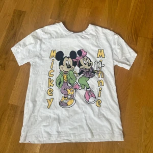 Disney t-shirt - Vit t-shirt från Xside x Disney i storlek XS med stort tryck av Mickey och Minnie Mouse i färgglada kläder. Klassisk passform och korta ärmar, perfekt för dig som älskar retro och Disney-vibes.