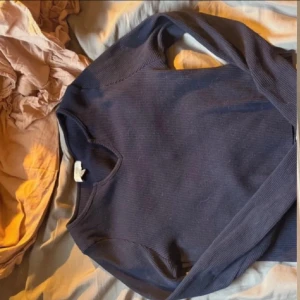 Mörkblå ribbad croppad tröja - Säljer en mörkblå ribbad tröja med v-ringning och croppad passform. Tröjan har långa ärmar och är tillverkad i ett stretchigt material som sitter snyggt på kroppen. Från pull & bear i storlek XL