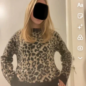 Leopardmönstrad stickad tröja - Säljer en snygg stickad tröja med leopardmönster i beige, svart och brunt. Tröjan har svarta muddar vid ärmslut och nederkant samt rund halsringning. Perfekt för dig som vill sticka ut lite extra med din outfit.
