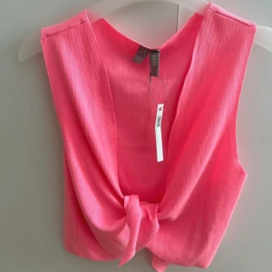 Rosa ribbad linnetopp från ASOS - Superfin rosa linnetopp från ASOS med ribbad struktur och knyt framtill. Toppen är ärmlös och croppad, perfekt för att skapa en cool och avslappnad look. Enkel att matcha med både jeans och kjol för en trendig stil