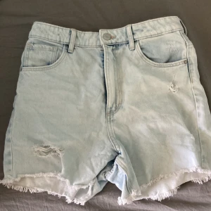 Ljusblåa jeansshorts med fransig kant - Snygga ljusblå jeansshorts med hög midja och slitna detaljer. Shortsen har fransig kant nertill, klassiska fickor fram och bak samt bälteshällor. Perfekta för sommardagar och ger en avslappnad vibe.