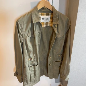 Olivgrön overshirt från Casual - Olivgrön overshirt med rutigt innerfoder från Casual by Lindex. Jackan har flera fickor framtill, knappar och klassisk krage. Perfekt för lager-på-lager och chill stil. Långärmad och i bomullsmaterial.