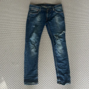Blå  jeans från Nudie Jeans - Säljer ett par blå jeans från Nudie Jeans i storlek 29/30. Jeansen har slitna detaljer och är i modellen tight terry.