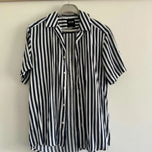 Randig skjorta från Only & Sons - Snygg skjorta från Only & Sons med vertikala svarta och vita ränder. Skjortan har korta ärmar, klassisk krage och knäppning framtill. Tillverkad i bomull för en skön och luftig känsla.