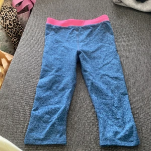 Blå sportleggings från H&M med rosa linning - Blåmelerade sportleggings från H&M med en snygg rosa linning. Modellen är trekvarts och har en liten slitsdetalj nertill på benen. Perfekta för träning eller chill. Gjorda i mjukt och stretchigt syntetmaterial för bästa komfort.