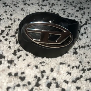 Vintage Diesel Belt  - Snyggt svart skärp från Diesel med ett ovalt, silverfärgat metallspänne och stilren design. Skärpet är gjort i slätt skinn och har flera hål för justerbar passform. Perfekt accessoar för att lyfta din outfit med en cool detalj.