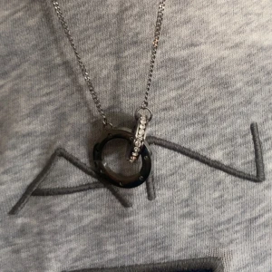 Silverfärgat halsband med ringar - Snyggt halsband i silverfärg med två runda hängen. Ena ringen är dekorerad med små stenar som glittrar och den andra har en cool, industriell look med nitar runt om. Kedjan är tunn och stilren.