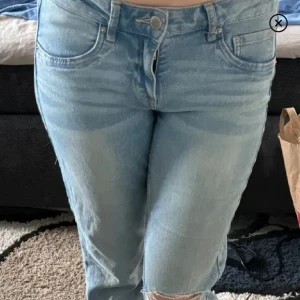 Ljusblå bootcut jeans med slitning - Säljer ett par ljusblå jeans med utsvängd passform och snygg slitning på ena knät. Perfekta för en avslappnad och trendig look. Inte min bild. Jeansen har slitits upp lite mellan låren, har därför sytt men de har slitits! 