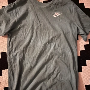 Grön Nike t-shirt i bomull - Snygg grön t-shirt från Nike med klassisk vit logga på bröstet. Skön passform och tillverkad i mjuk bomull. Perfekt för en chill och sportig stil. Rund halsringning och korta ärmar gör den enkel att matcha med jeans eller shorts.