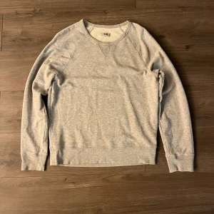 Grå sweatshirt från Acne Studios - En stilren ljusgrå sweatshirt från Acne Studios i storlek S. Tröjan har rund halsringning, raglanärmar och breda muddar vid ärmslut och nederkant. Tillverkad i mjuk bomull för en skön och avslappnad look.
