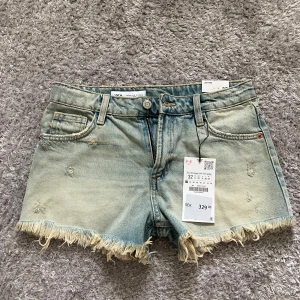 Lågmidjade jeansshorts från Zara - Snygga ljusblå jeansshorts från Zara med låg midja, slitna detaljer och fransig kant nedtill. Klassisk femficksmodell med dragkedja och knapp. Perfekta för en chill sommarlook.