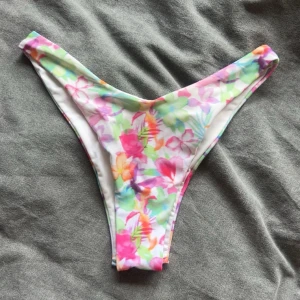 Blommig bikiniunderdelar  - Snygga bikiniunderdelar med blommigt mönster i pastelliga färger som rosa, grön, blå, orange och lila. Modellen är högt skuren och har en v-formlig modell.