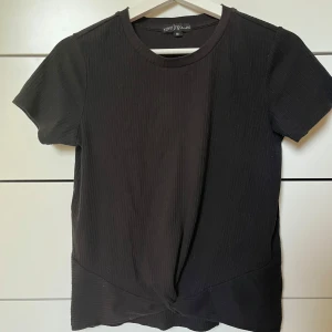 Svart ribbad topp med twist  - Svart ribbad topp från gekås med kort ärm och rund hals. Snygg twistad detalj framtill som ger en cool look. Mjuk och stretchig, perfekt till jeans eller kjol. Enkel att styla och passar året runt. Köpt från barnavdelningen (stl 170) men passar mig bra som oftast bär S. Skriv om ni har några frågor💞🤗