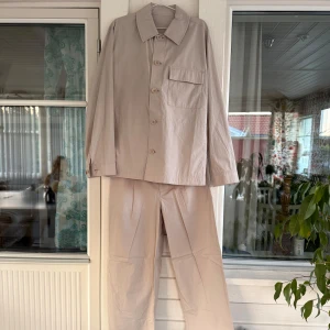 Arket Beige set - Stilrent beige lätt, luftigt, och svalt bomulls set med rak passform i mjuk bomull från Arket. Perfekt till sommaren. Skjortan har klassisk krage, knäppning framtill och bröstficka med lock. Byxorna har raka ben och fickor med lock bak. Perfekt för dig som gillar minimalistisk och clean stil. Skick som nytt endast testat. Byxor storlek 48. Skjorta storlek 50. 
