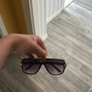 Väldigt lika carrera solglasögon  - Snygga solglasögon med svarta pilotbågar och guldiga detaljer på sidorna och upptill. Glasen är mörka och ger en cool vibe, perfekt för att sticka ut i sommar. Klassisk och trendig design som passar till många outfits.