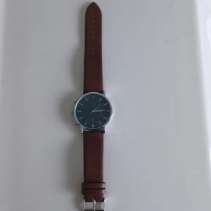 Pier One klocka med brunt läderband - Stilren klocka från Pier One med mörkblå urtavla och silverfärgat hölje. Klockan har ett klassiskt brunt äkkta läderband och enkla indexmarkeringar. Perfekt accessoar för dig som gillar en clean look och snygga detaljer.