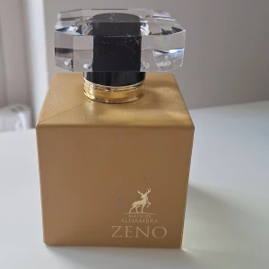 Zeno Maison Alhambra parfym 100 ml - Lyxig parfym för kvinnor från Maison Alhambra, Zeno. Flaskan är fyrkantig i guld med transparent botten och har en stor, kristalliknande kork. Doften har träiga, citrus, blommiga och aromatiska toner. Perfekt för dig som gillar eleganta och fräscha dofter. (Enbart testad)