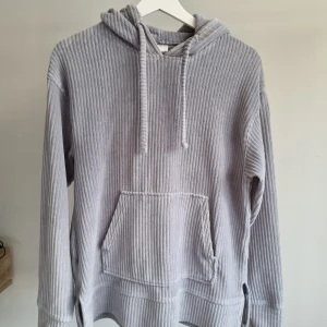 Duvblå ribbad hoodie från Kappahl - Mysig ljus gråblå hoodie från Kappahl i ribbad manchester-look. Tröjan har huva med snörning, känguruficka och långa ärmar. Perfekt för chill dagar eller när du vill ha en avslappnad stil.