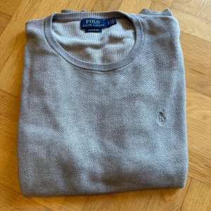 Grå bomullströja från Polo Ralph Lauren - Snygg grå tröja från Polo Ralph Lauren i mjuk pima bomull. Klassisk rund halsringning, diskret broderad logga på bröstet och ribbade muddar. Perfekt för dig som gillar stilren och enkel design med premiumkänsla.