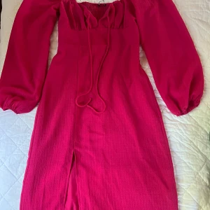 Ceriserosa långklänning från Gina Tricot - Superfin ceriserosa långklänning från Gina Tricot med puffiga långärmar, smockad rygg och snörning vid halsen. Klänningen har en slits framtill och är i ett lätt, vävt material som känns luftigt och bekvämt. Storlek 36 helt ny använt en gång 