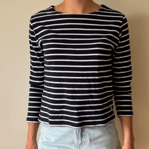 Randig trekvarts tröja  - Snygg långärmad tröja med marinblå och vita horisontella ränder. Tröjan har en rak passform, rund halsringning och är tillverkad i mjuk bomull. Perfekt för en chill och stilren look.