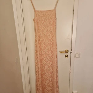 Ljusrosa långklänning från NA-KD - Superfin ljusrosa långklänning från NA-KD med tunna axelband och blommigt spetsmönster. Klänningen har en rak passform och är perfekt för sommarens alla tillfällen. Materialet känns lätt och luftigt. Ser mer babyrosa ut i verkligheten 