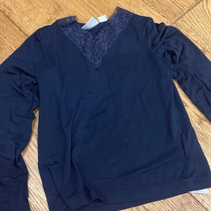 Mörkblå långärmad topp med spets - Mörkblå långärmad topp från Gina Tricot med snygg v-ringning och spetsdetalj framtill. Tunn och mjuk, perfekt för lager-på-lager. Enkel men ändå med en extra touch tack vare spetsen vid halsen.