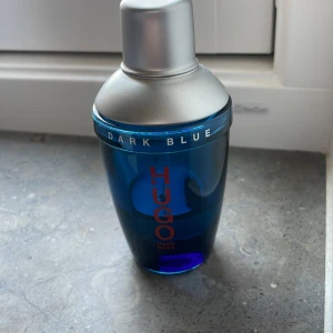 Hugo Boss Dark Blue parfym - Snygg parfymflaska från Hugo Boss i modellen Dark Blue. Flaskan är djupblå med silverfärgat lock och har röd logotyp framtill. Modern och stilren design som sticker ut i badrumshyllan. Perfekt för dig som gillar klassiska dofter med en twist.
