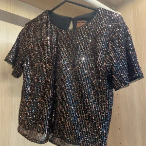 Snygg Svart fest paljettopp - Glittrig svart topp köpt utomlands, täckt med paljetter i olika färger, perfekt för en fest. Modellen har rund halsringning och korta ärmar samt är lite kroppad. Jätte skön och snygg.  Passar xs, s och m beroende på önskad passform