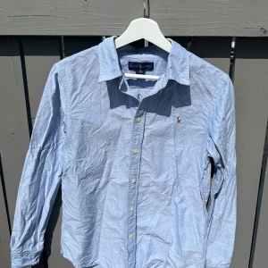Blå skjorta från Ralph Lauren - Blå skjorta från Ralph Lauren i barnstorlek 18 vilket motsvarar S. Riktigt fräsch till sommaren och i bra skick. Tveka inte på att skicka frågor eller funderingar!