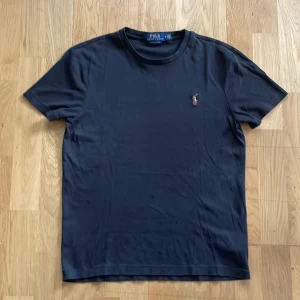 Mörkblå t-shirt från Polo Ralph Lauren - Snygg mörkblå t-shirt från Polo Ralph Lauren med klassisk broderad logga på bröstet. Modellen är slim fit och har rund halsringning samt korta ärmar. Perfekt för en clean och stilren look.