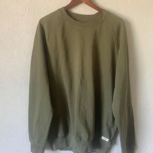 Olivgrön sweatshirt från 157, XXL - Olivgrön sweatshirt från 157 i storlek XXL. Tröjan har rund halsringning, ribbade muddar och är tillverkad i mjuk bomullsmix. Enkel och stilren design som passar perfekt till jeans eller joggers.