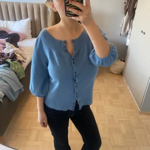 Kashmir kofta - Superfin ljusblå 100% Kashmir kofta med trekvartsärmar och snygga knappar hela vägen framtill. Koftan har bred ribbad kant vid halsen och nederkanten, vilket ger en chill och modern look. Perfekt att slänga på sig över ett linne eller t-shirt.