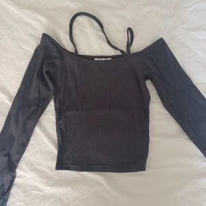 Mörkgrå offshoulder topp från Lewkin - Säljer en mörkgrå ribbad offshoulder topp från Lewkin. Toppen har långa ärmar och smala axelband som ger en snygg och trendig look. Perfekt för dig som gillar stilrena och moderna plagg med en twist.