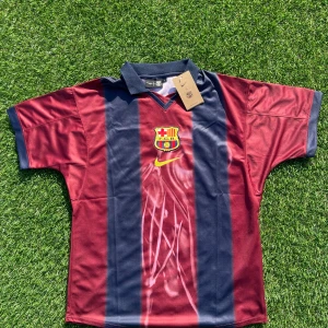 Barça x Cactus Jack Nike fotbollströja L - Snygg FC Barcelona fotbollströja i samarbete med Cactus Jack och Nike. Tröjan är randig i vinrött och marinblått med klubbmärke och gul Nike-logga på bröstet. På ryggen står det 'Cactus Jack', nummer 2 och 'BARÇA'. Tillverkad i lätt och ventilerande polyester.
