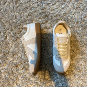 Maison Margiela vita sneakers i skinn - Maison Margiela sneakers i vitt och beige med klassisk gummisula. Ovandel i skinn och mocka. Perfekta för dig som gillar stilrena och trendiga sneakers med premiumkänsla.                                               Om du har nån fråga e de bara att skriva.            Boxen och en påse kommer med 