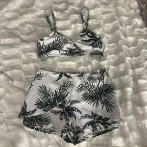 Vit bikini med palmbladsmönster - Snygg bikini med vit bas och grönt palmbladsmönster. Toppen har smala axelband och byxorna är höga med shortsmodell för extra komfort. Perfekt för strandhäng och poolparty. Materialet känns som syntet, vilket torkar snabbt och är bekvämt att bära. Justerbara axlar och går att sätta in inlägg ifall man vill. Storlek xxs men ingen lapp på. Från shein men den är som en helt vanling bikini!