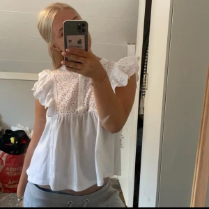 Vit blus med volangärmar - Supersöt vit blus med broderade detaljer och volangiga ärmar. Blusen har en luftig passform och knappar framtill. Perfekt för dig som gillar romantisk och feminin stil.