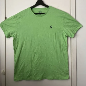 Grön t-shirt från Polo Ralph Lauren - Snygg ljusgrön t-shirt från Polo Ralph Lauren med klassisk rund hals och broderad marinblå logga på bröstet. Tillverkad i mjuk bomull som känns skön mot huden. Perfekt för dig som gillar stilrena och fräscha plagg med en sportig touch.