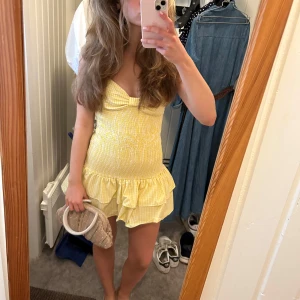 Gul-rutig kortklänning med rosett - Supersöt gul och vit rutig kortklänning med smockad midja, volangkant och smala axelband. Klänningen har en öppen rygg med knytning. Endast använd en gång. Från zara och slutat tillverkas.