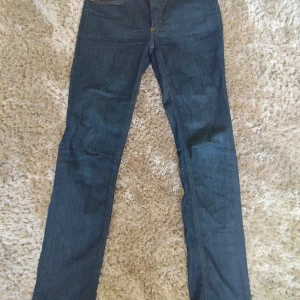 Mörkblå jeans från Acne Studios - Snygga mörkblå jeans från Acne Studios med klassisk femficksdesign och raka ben. Jeansen har orangea kontrastsömmar och läderpatch bak i midjan. Perfekta för dig som gillar stilrena och tidlösa jeans med en clean look.