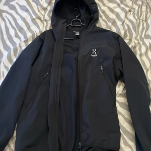 Svart jacka från Haglöfs - Säljer en svart jacka från Haglöfs med huva och dragkedja. Jackan har en stilren design med .logotyp. Säljer då jag ska byta stil. 800