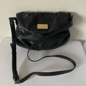 Svart axelremsväska med justerbar rem - Svart axelremsväska i skinnimitation med justerbar rem och magnetlås. Väskan har flera fack inuti, inklusive ett med dragkedja.