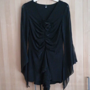 Svart klänning från ZARA - Elegant svart klänning från ZARA med långa ärmar och en v-ringad design. Klänningen har en dekorativ blomdetalj framtill och ett flödande tyg som ger en fin siluett. Perfekt för en stilfull look.