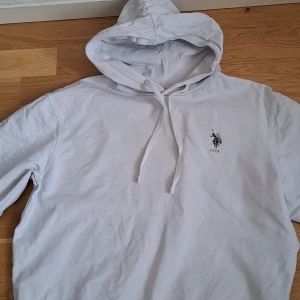 Vit hoodie från U.S. Polo Assn. - Säljer en klassisk vit hoodie från U.S. Polo Assn. med en broderad logga på bröstet. Tröjan har en justerbar huva med dragsko och är perfekt för en avslappnad stil.